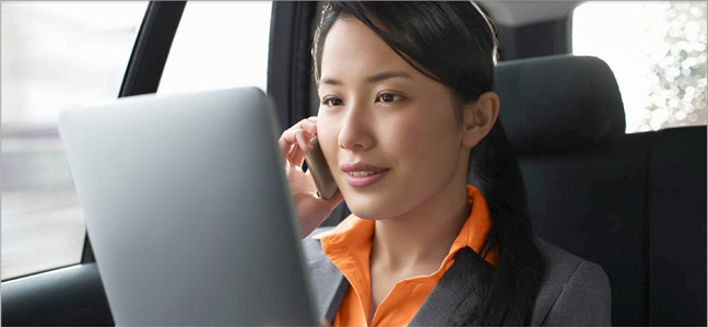 consultas internacional Fotografia de uma mulher dentro de um carro utilizando os seu celular e o seu computador.