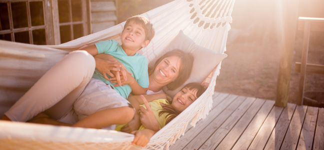 Proteja sua família Fotografia de uma mãe com os seus dois filhos deitados em uma rede.