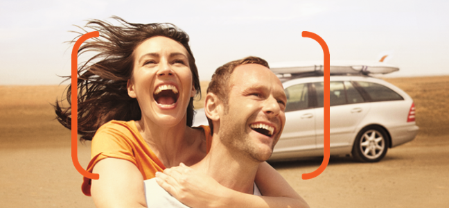 Conheça o seguro de carro Itaú Fotografia de um casal sorrindo com um automóvel parado ao fundo.